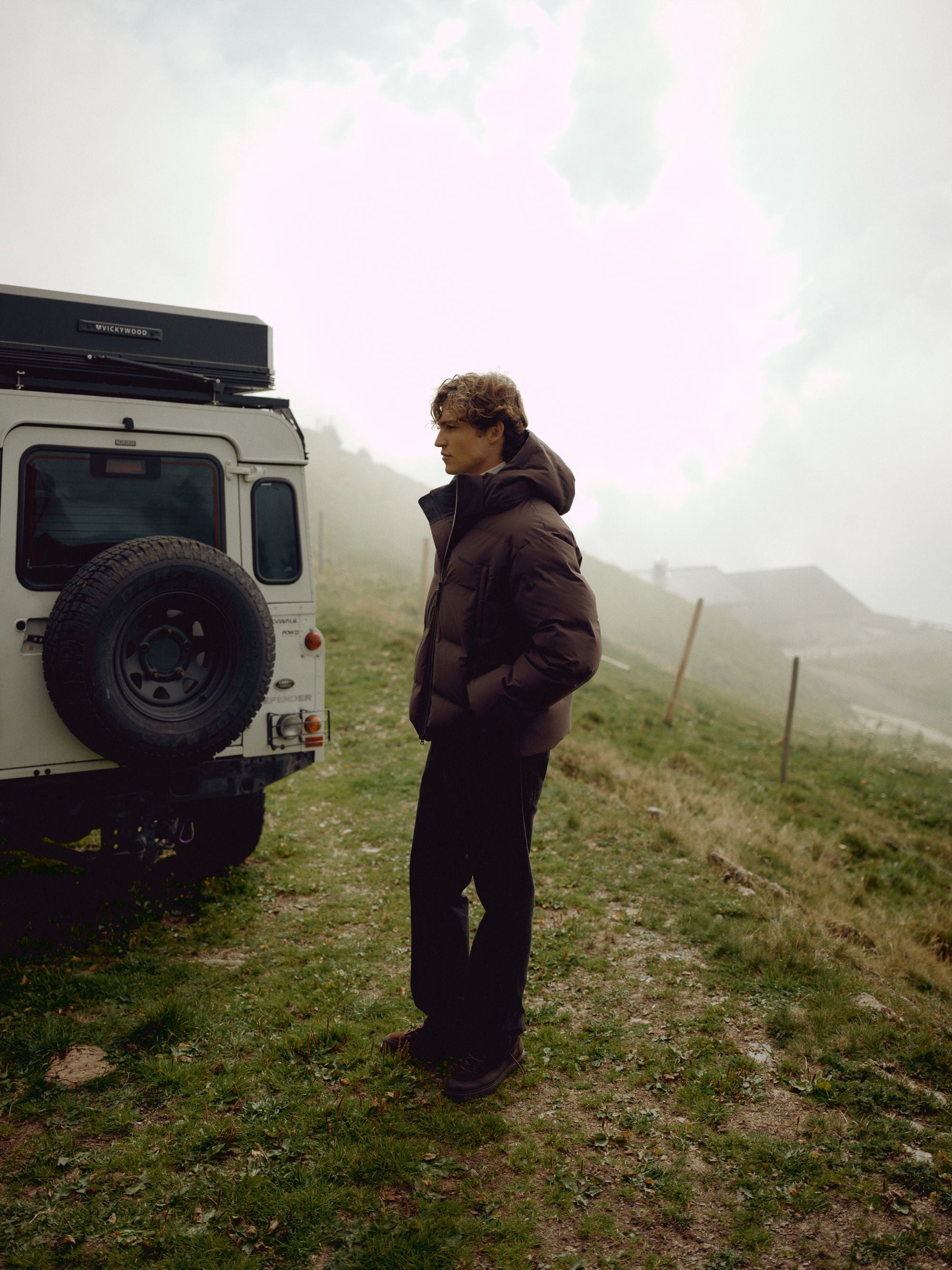 Man wearing a cocoa bean CASPARA Boreal puffer jacket outdoors next to an off-road vehicle.